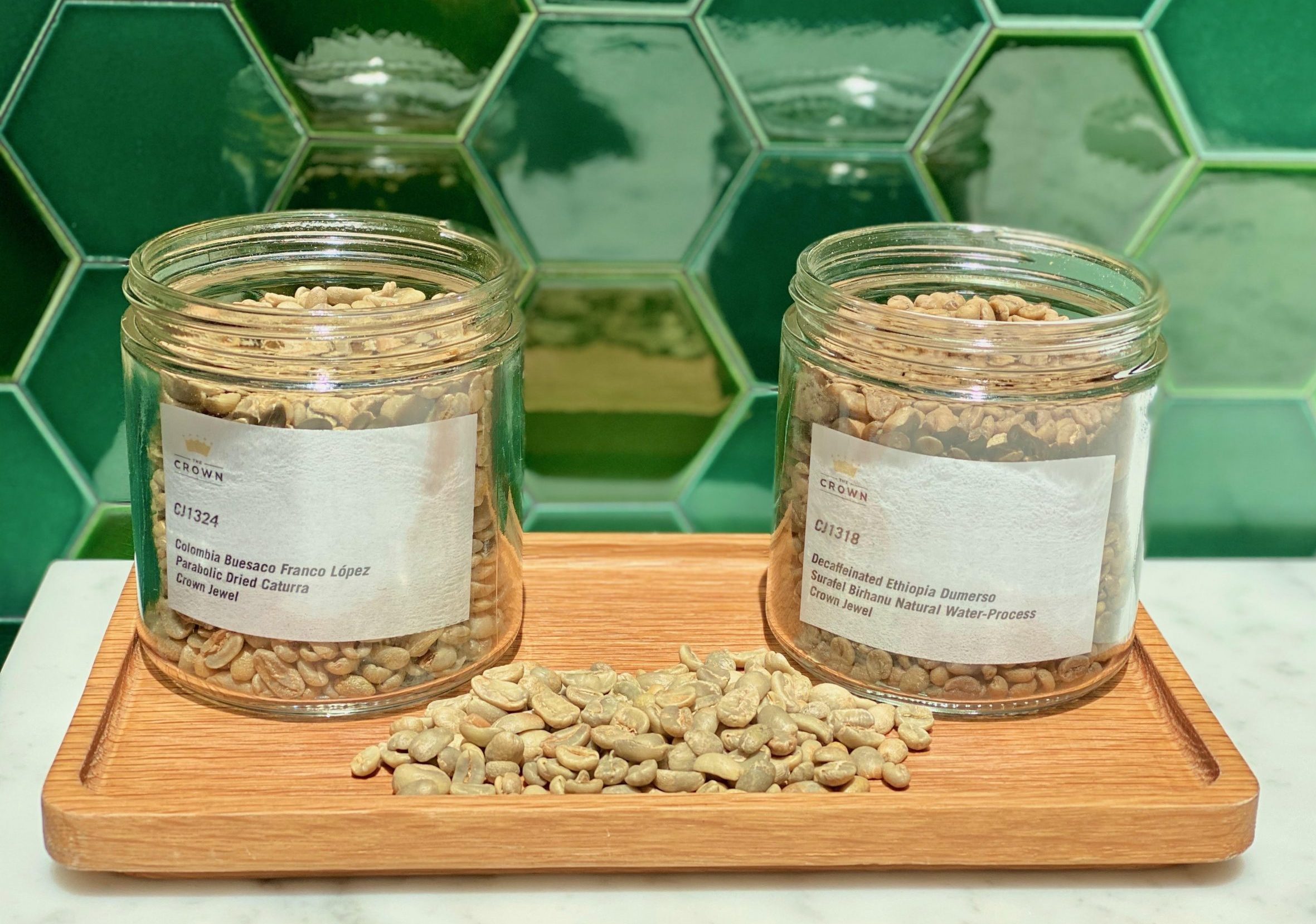 Two glass jars filled with light-colored coffee beans sitting on a wooden tray